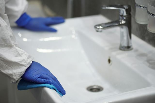 person in blue plastic gloves cleaning a sink